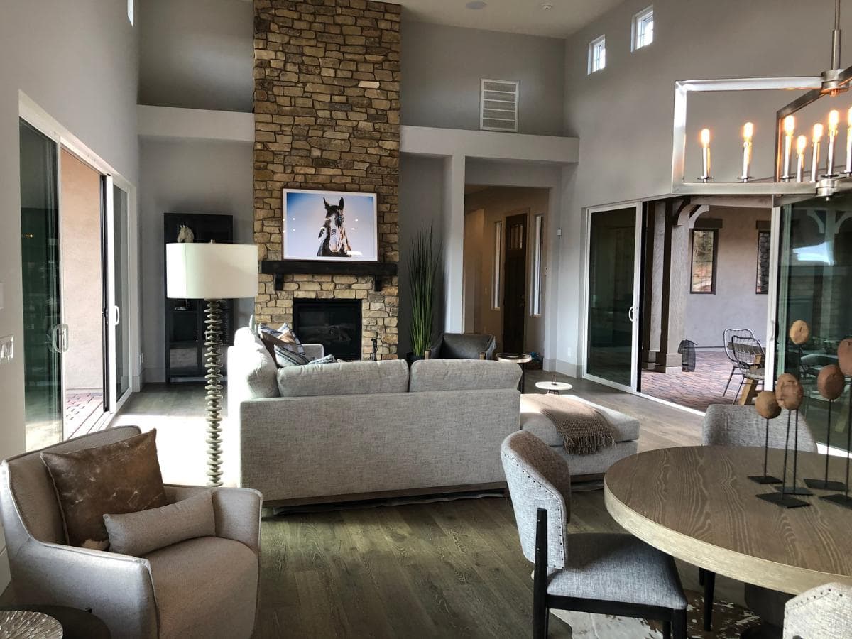 A modern open-concept living room with a floor-to-ceiling stone fireplace and large sliding glass doors, designed by Sedona Interior Designer Dana Cavanaugh to showcase biophilic design and natural lighting.
