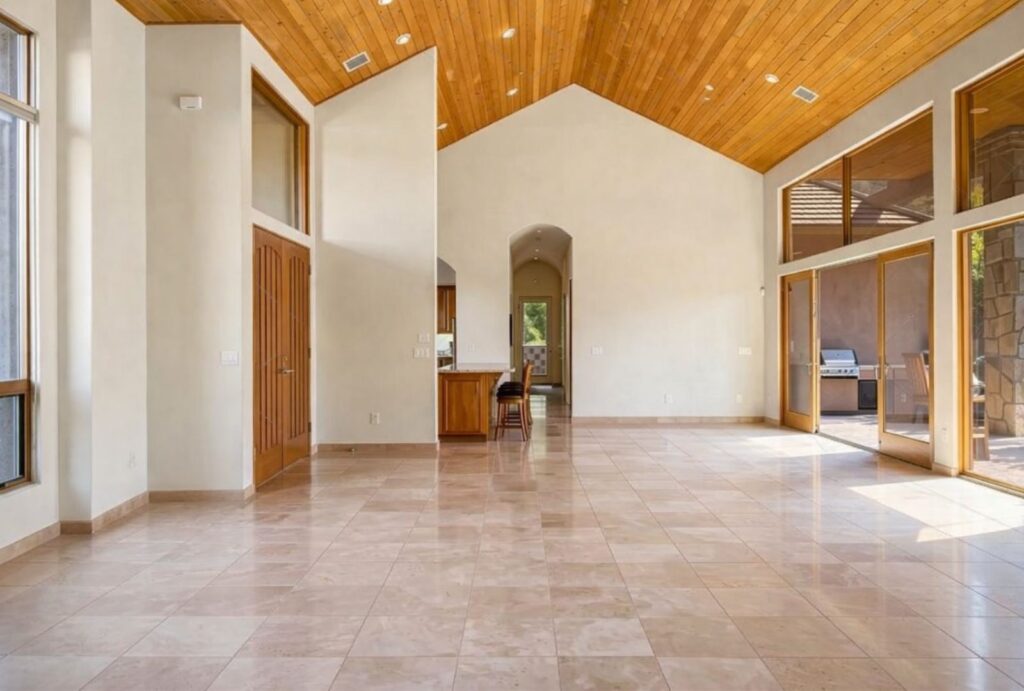 An expansive, empty living and dining area with a vaulted wood-plank ceiling and travertine floors, used as a canvas for biophilic design by Sedona Interior Designer Dana Cavanaugh.